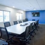 conference room with one blue wall, long white table, black office chairs, and tv