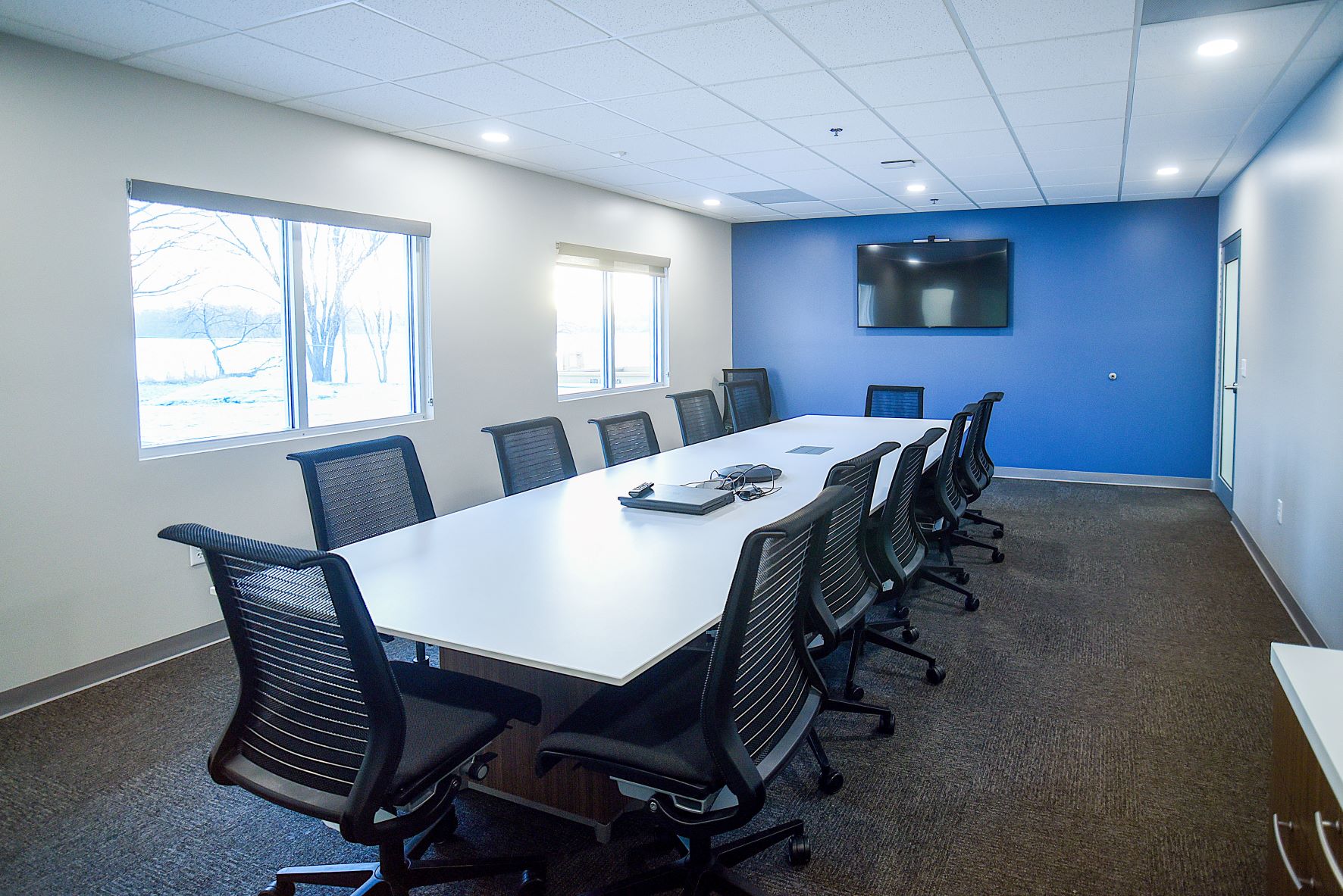 conference room with one blue wall, long white table, black office chairs, and tv
