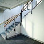 carpeted office staircase with wooden railing and drop ceiling