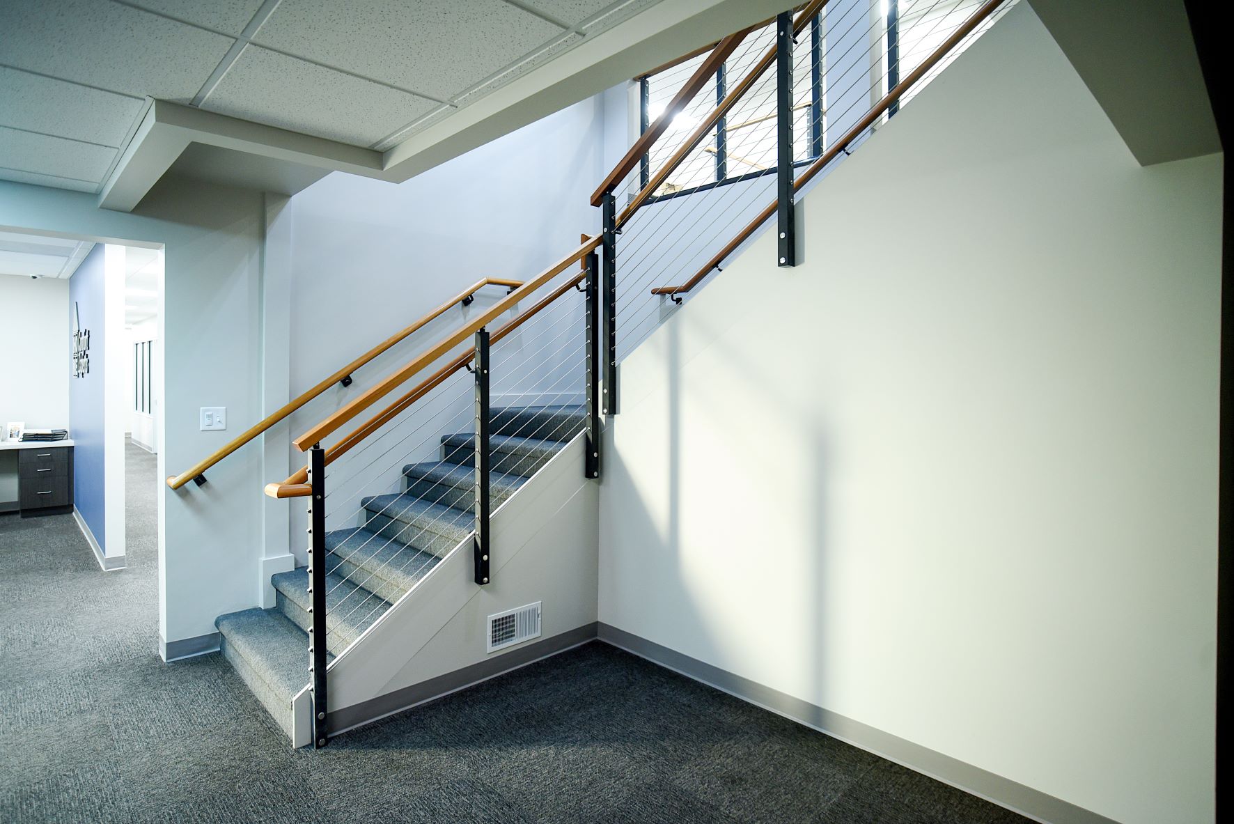 carpeted office staircase with wooden railing and drop ceiling