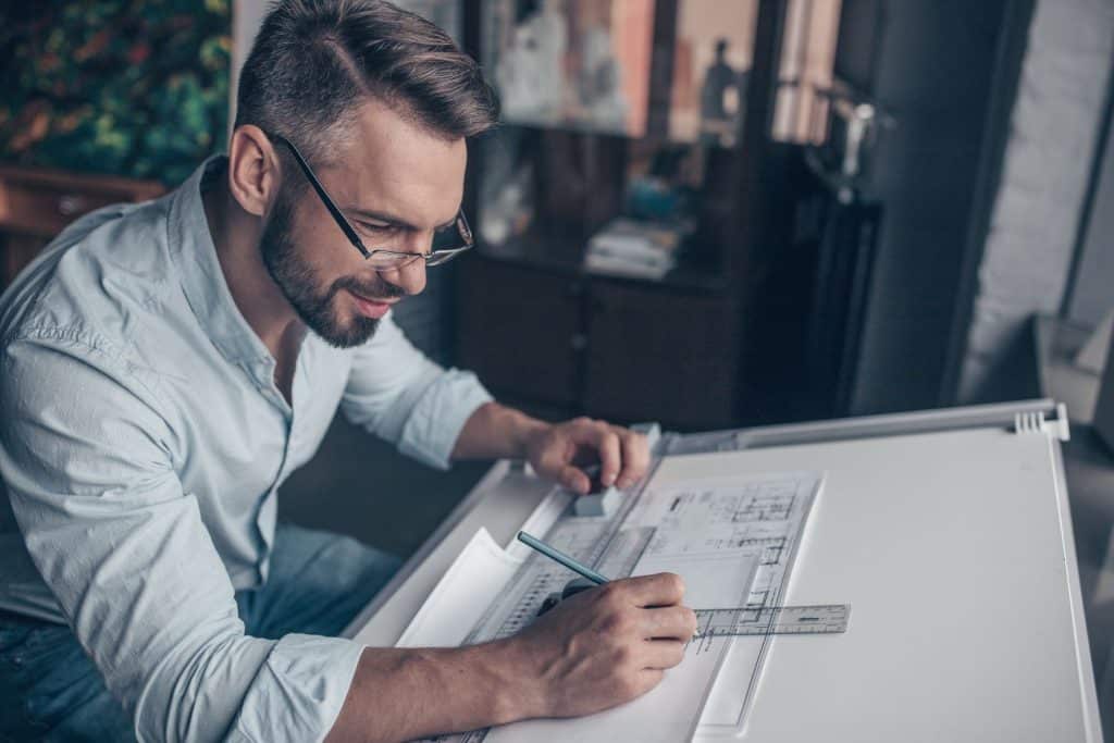 smiling male architect drafting drawings with pencil and ruler at his desk