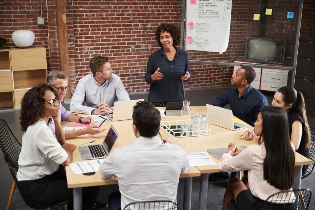 Mature Businesswoman Standing And Leading Office Meeting Around Table