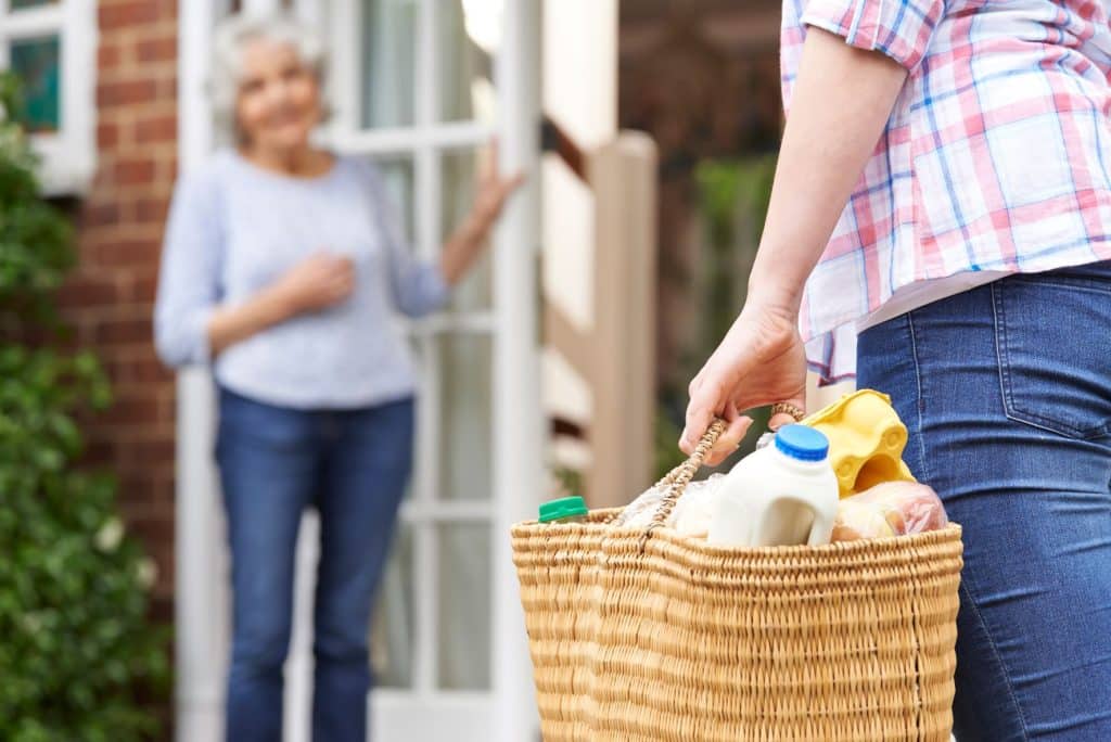 person bringing elderly neighbor a basket of groceries