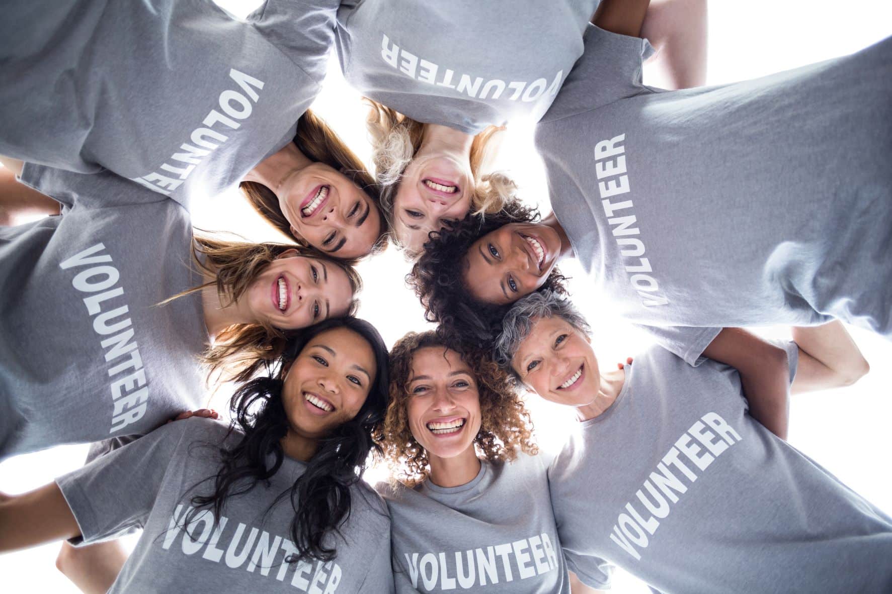 Happy diverse group of women forming a huddle, all wearing volunteer t-shirts