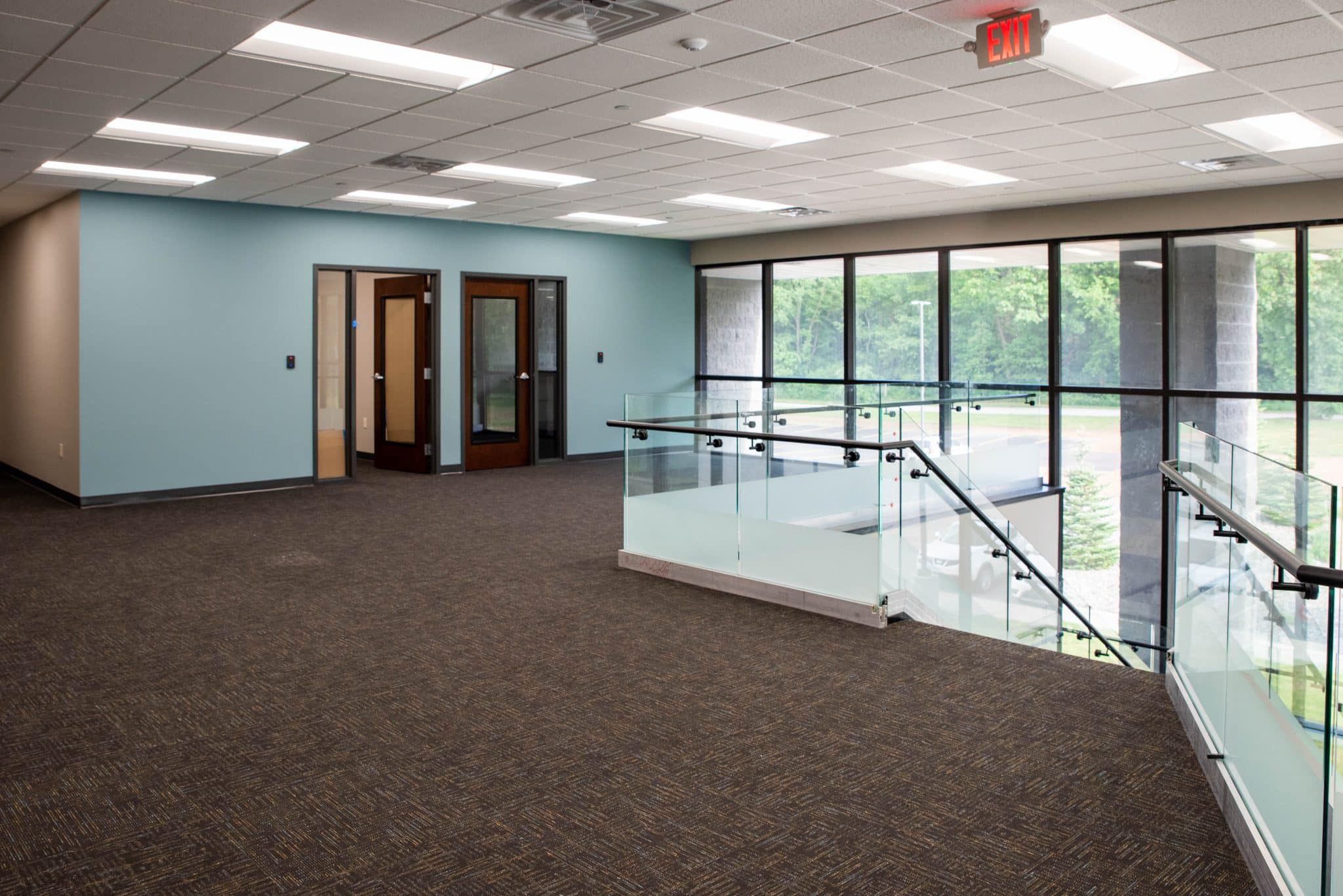 office landing with turquoise walls, large windows, and glass staircase railing