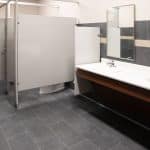 men's restroom with slate tile, two sinks, and gray partitions