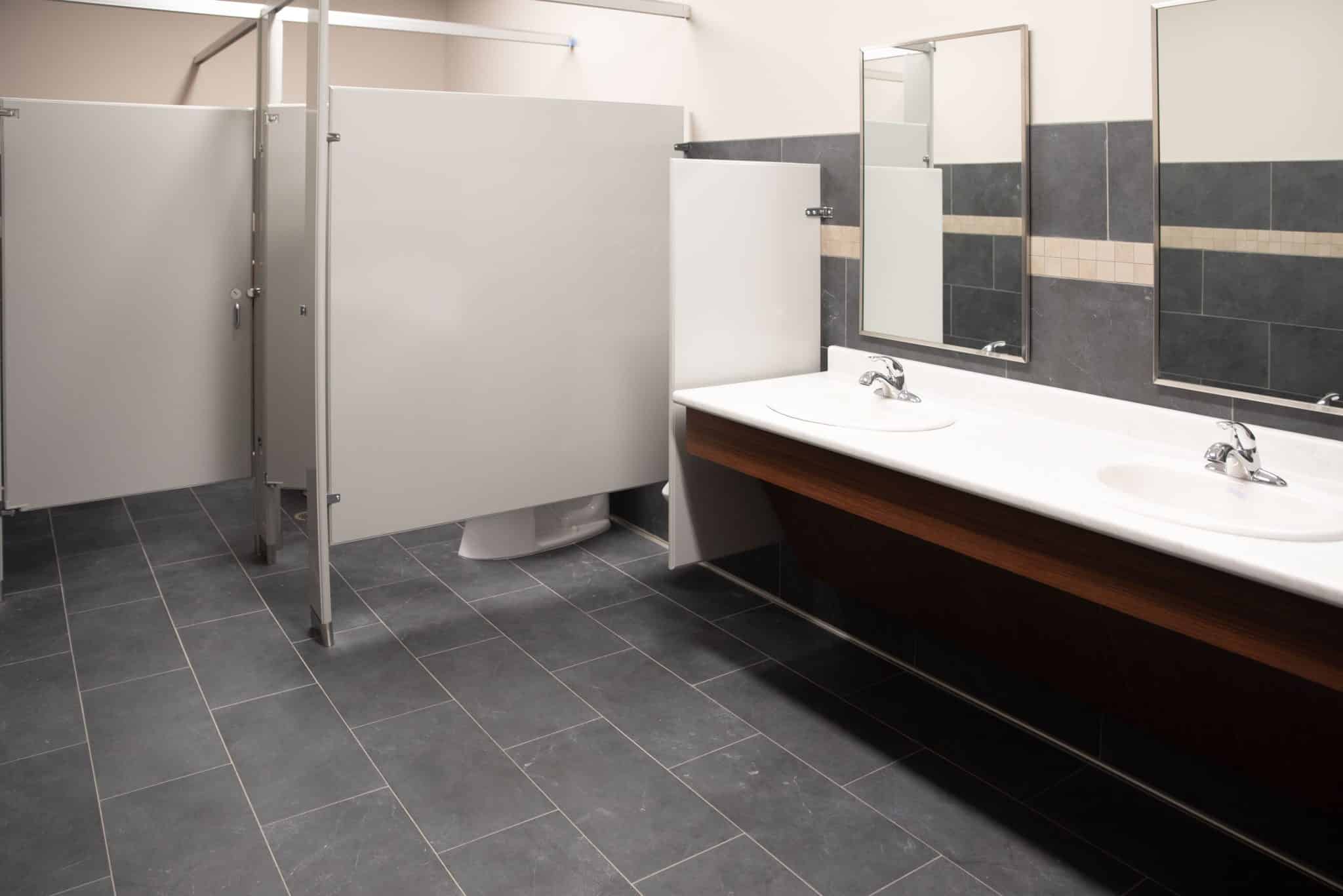 men's restroom with slate tile, two sinks, and gray partitions