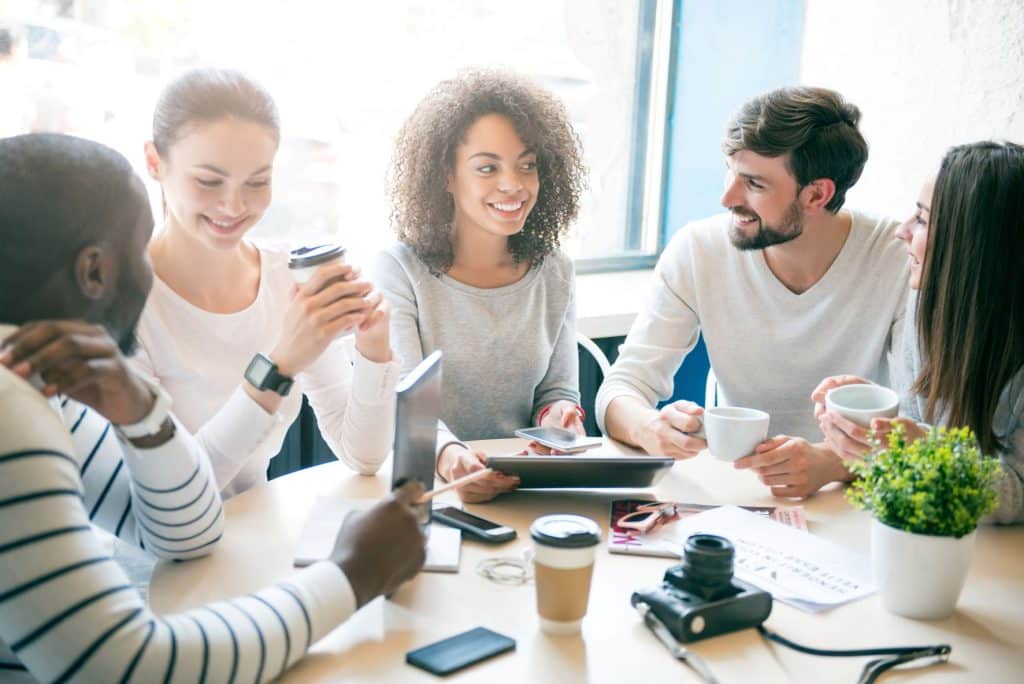 diverse group of young adults sitting at a table talking and drinking coffee