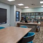 large office with bookshelves on one wall, L-shaped desk, and conference table