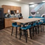 office break room with a fridge, a small kitchenette, a table with stools, and a couch