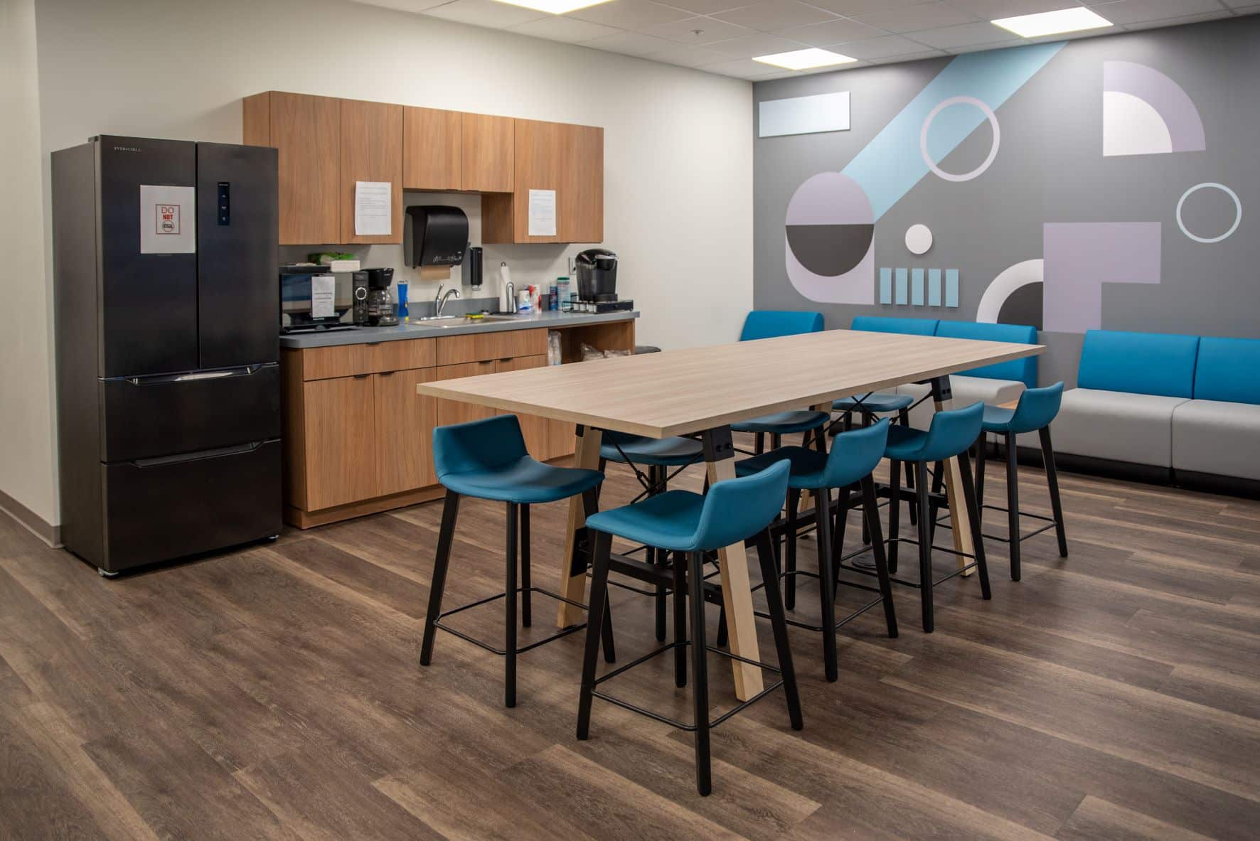 office break room with a fridge, a small kitchenette, a table with stools, and a couch