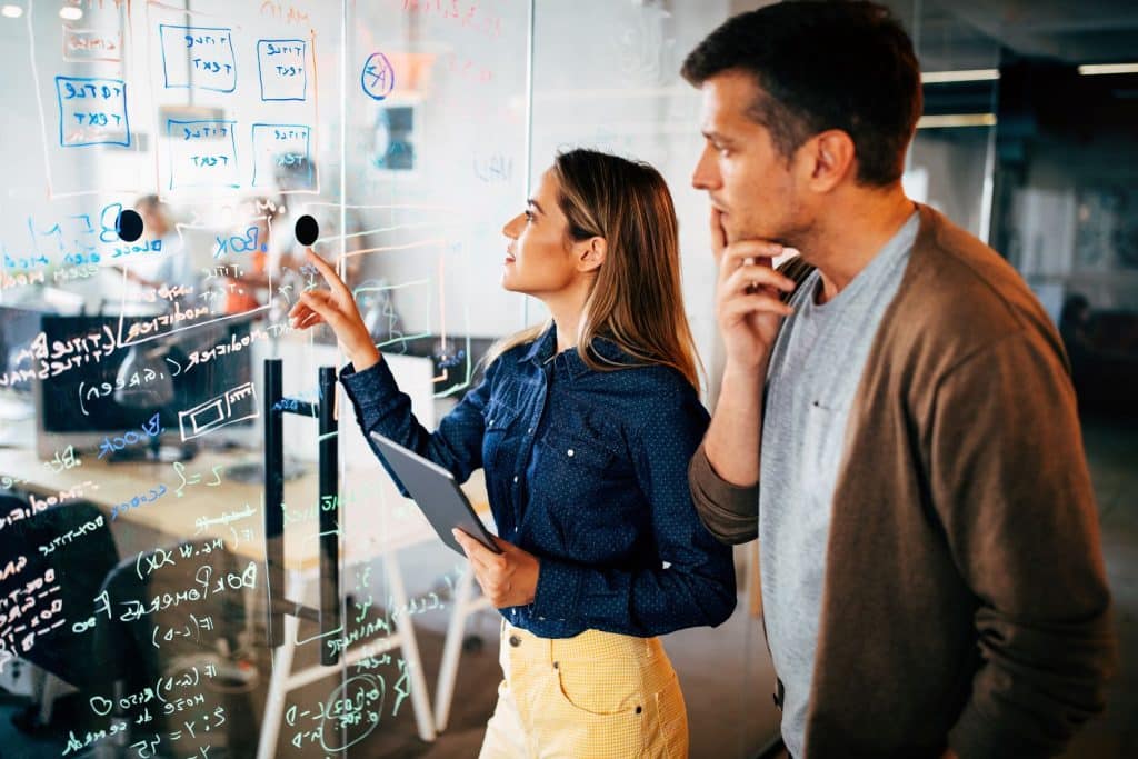 two colleagues brainstorming in office with whiteboard