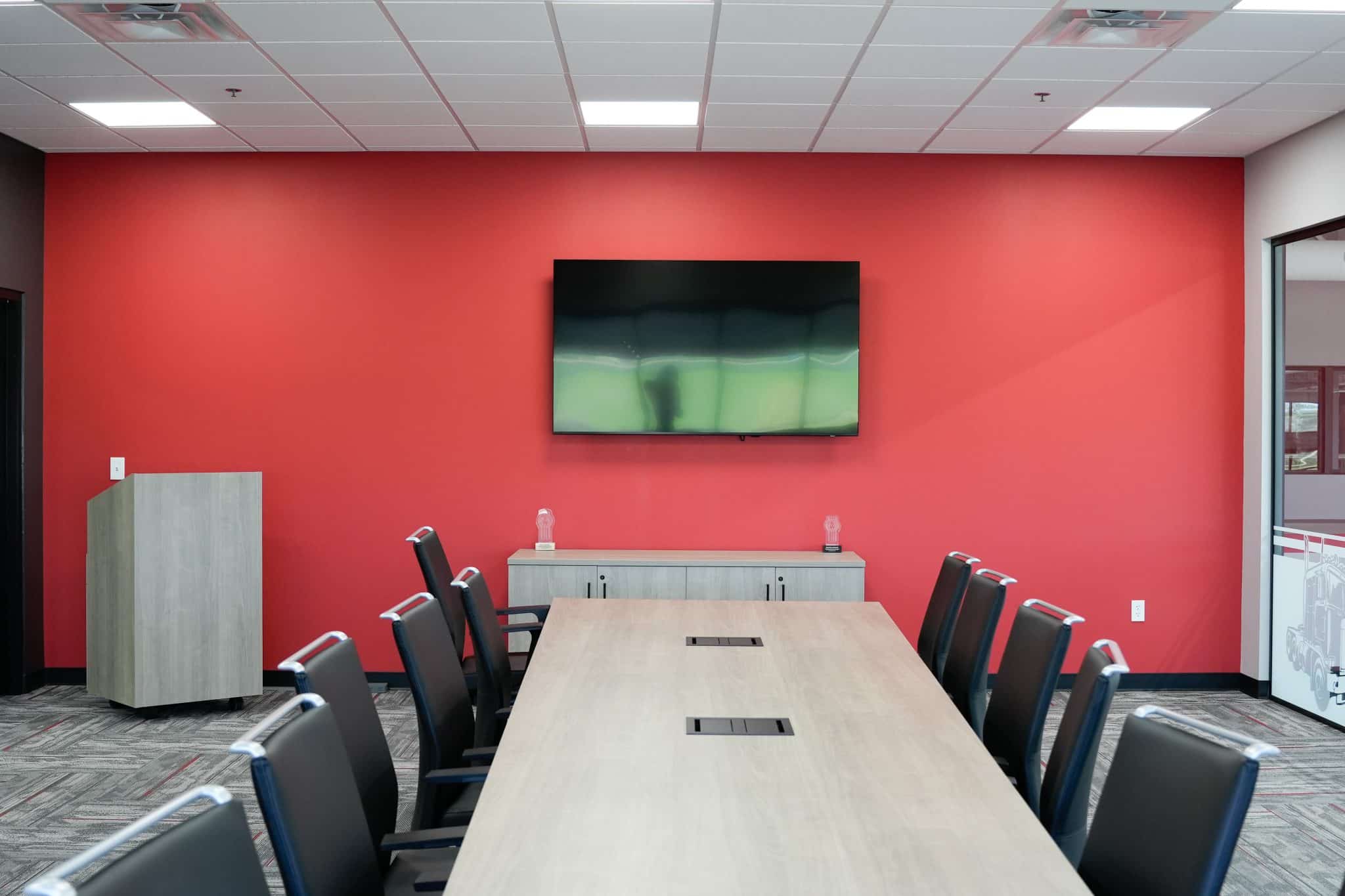 Boardroom at Whiteford Kenworth Toledo featuring red wall, mounted TV, and modern meeting table with chairs.